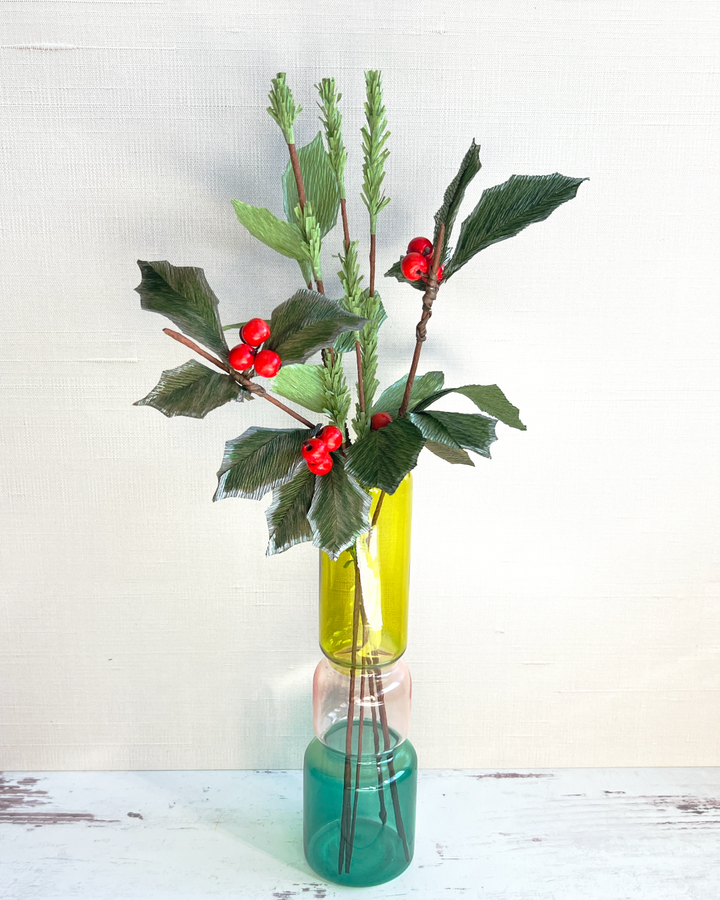 a green vase with red berries and green leaves