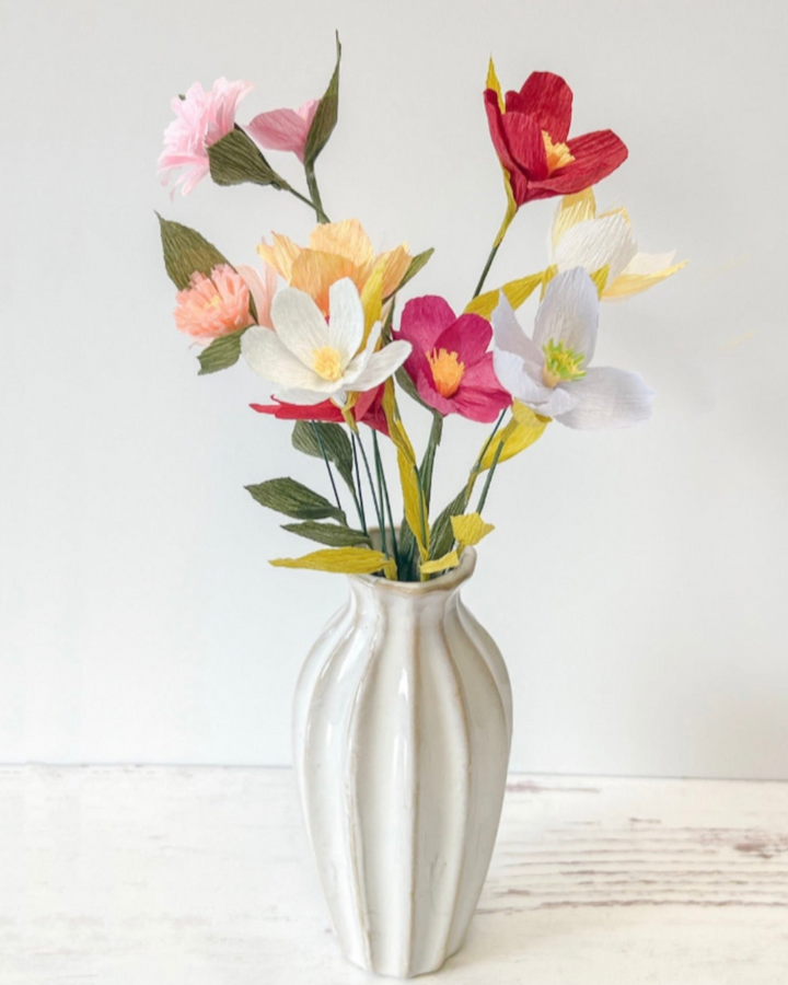 a white vase filled with colorful flowers on top of a table