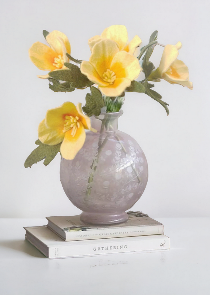 a gray vase with yellow flowers on top of a stack of books